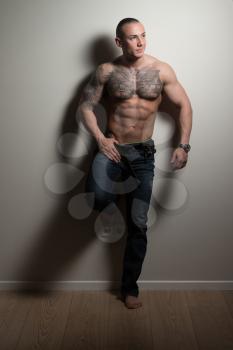 Portrait of a Tattoo Man In Jeans Showing His Abs Standing Isolated on Gray Background