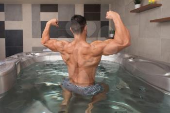 Wellness Spa - Man Flexing Muscles in Hot Tub Whirlpool Jacuzzi Indoors at Luxury Resort Spa Retreat - Handsome Young Male Model Standing Strong in Water Near Pool on Travel Vacation Holiday