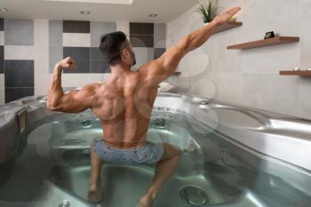 Wellness Spa - Man Flexing Muscles in Hot Tub Whirlpool Jacuzzi Indoors at Luxury Resort Spa Retreat - Handsome Young Male Model Standing Strong in Water Near Pool on Travel Vacation Holiday