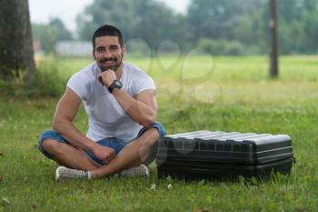 Portrait of Confident Young Engineer Sitting On Grass With Case from Drone