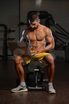 Resting Time - Confident Muscled Young Man Resting In Healthy Club Gym And Using Laptop