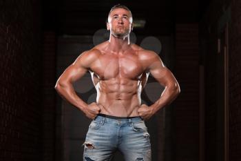 Healthy Young Man In Jeans Standing Strong In The Gym And Flexing Muscles - Muscular Athletic Bodybuilder Fitness Model Posing After Exercises