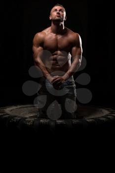 Portrait Of A Young Physically Fit Man Workout At Gym With Hammer - Muscular Athletic Bodybuilder Fitness Model Posing After Exercises On Tractor Tire