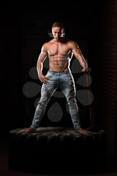 Portrait Of A Young Physically Fit Man Workout At Gym With Hammer - Muscular Athletic Bodybuilder Fitness Model Posing After Exercises On Tractor Tire