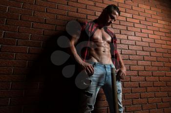 Healthy Young Man Standing Strong In The Gym And Flexing Muscles While Wearing Plaid Shirt - Muscular Athletic Bodybuilder Fitness Model Posing After Exercises On Wall of Bricks