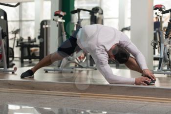 Muscular Man Stretches At The Floor In A Gym And Flexing Muscles - Muscular Athletic Bodybuilder Fitness Model