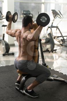 Strong Man In The Gym And Exercising Shoulders With Dumbbells - Muscular Athletic Bodybuilder Fitness Model Exercise Shoulder