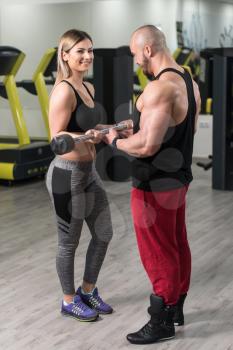 Strong Young Couple Doing Exercise For Biceps With Barbell In The Gym