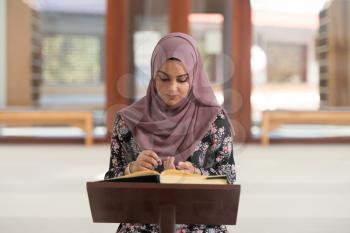 Muslim Woman Making Traditional Prayer To God While Reading The Quran In Mosque