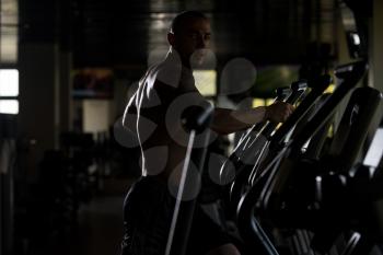 Muscular Young Man Doing Aerobics Elliptical Walker In Modern Fitness Center