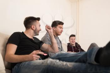 Three Brothers or Friends Playing Video Games Together as They Relax on a Couch in the Living Room