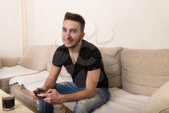 Young Gamer Sitting On Sofa And Playing Video Games At Home