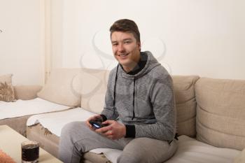 Young Gamer Sitting On Sofa And Playing Video Games At Home