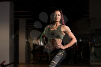 Attractive Young Woman Standing Strong In The Gym And Flexing Muscles - Beautiful Athletic Fitness Model Posing After Exercises