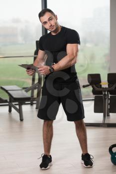 Personal Trainer Takes Notes On Clipboard In Fitness Center Gym