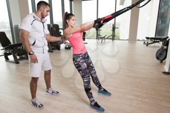 Personal Trainer Showing Young Woman How To Train With Trx Fitness Straps In The Gym