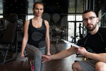 Young Woman And Personal Trainer With Dumbbells Flexing Muscles In Gym