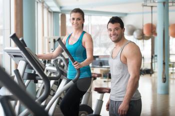 Group Of People Exercising On Elliptical Walker In Gym Or Fitness Club While Personal Trainer With Clipboard Watching Them - Group Of Woman And Men Exercising To Gain More Fitness