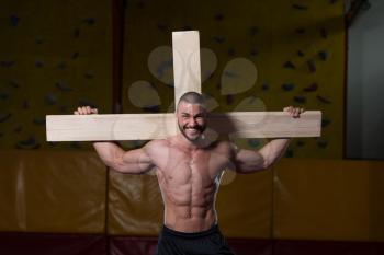 Portrait Of A Young Physically Fit Man Dragging a Wooden Cross In A Gym - Muscular Athletic Bodybuilder Fitness Model Posing After Exercises