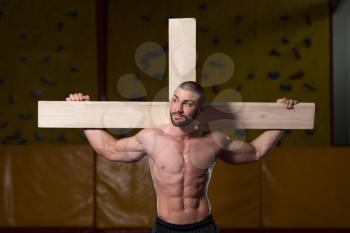 Portrait Of A Young Physically Fit Man Dragging a Wooden Cross In A Gym - Muscular Athletic Bodybuilder Fitness Model Posing After Exercises
