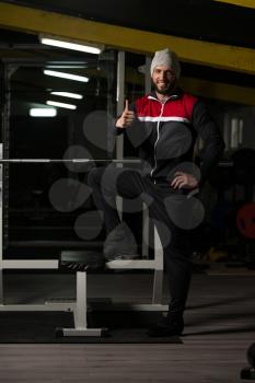 Portrait Of A Physically Fit Man In Track Suit Resting His Well Trained Body Showing Thumbs Up - Muscular Athletic Bodybuilder Fitness Model Posing After Exercises
