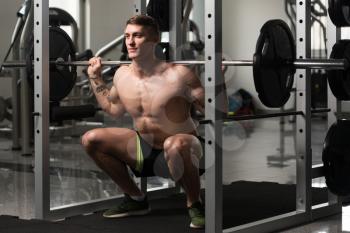 Healthy Fitness Man Working Out Legs With Barbell In A Gym - Squat Exercise