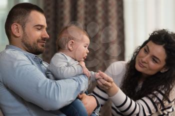 Relaxed Young Couple With Cute Little Baby Sitting on Couch Playing and Laughing
