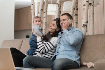Relaxed Young Father on the Phone Working and Mother With Cute Little Baby Sitting on Couch Playing and Laughing