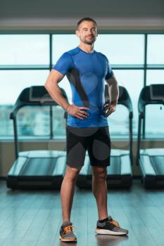 Personal Trainer Standing Strong In Fitness Centar - Gym Background With Copyspace And Flexing Muscles - Muscular Athletic Man Posing