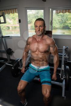 Handsome Muscular Fitness Bodybuilder Doing Heavy Weight Exercise For Trapezius On Machine In The Gym