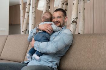 Happy Father Playing With a Baby at Home on the Sofa