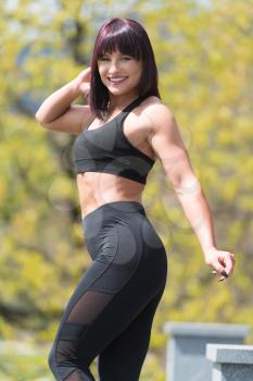 Attractive Young Woman Standing Strong Outdoors And Flexing Muscles - Beautiful Athletic Fitness Model Posing After Exercises