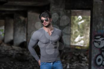 Portrait of a Young Physically Fit Man in Grey Long Sleeve Shirt Showing His Well Trained Body - Muscular Athletic Bodybuilder Fitness Model Posing After Exercises In Front Of A Graffiti Wall