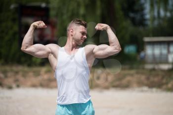 Handsome Young Man Standing Strong Outdoors And Flexing Muscles - Muscular Athletic Bodybuilder Fitness Model Posing After Exercises