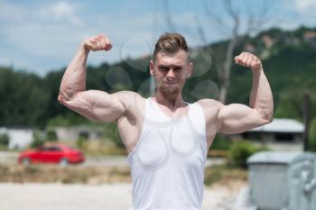 Healthy Young Man Standing Strong Outdoors  And Flexing Muscles - Muscular Athletic Bodybuilder Fitness Model Posing After Exercises
