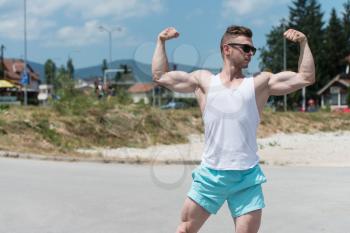 Handsome Young Man Standing Strong Outdoors And Flexing Muscles - Muscular Athletic Bodybuilder Fitness Model Posing After Exercises