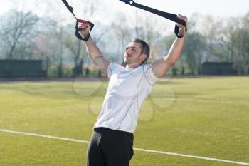 Young Man Doing Crossfit With Trx Fitness Straps in City Park Area - Training and Exercising for Endurance - Healthy Lifestyle Concept Outdoor