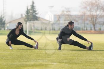 Young Couple Stretching Before Running In City Park Area - Training And Exercising For Trail Run Marathon Endurance - Fitness Healthy Lifestyle Concept Outdoor