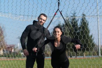 Attractive Couple Doing Crossfit With Trx Fitness Straps in City Park Area - Training and Exercising for Endurance - Healthy Lifestyle Concept Outdoor