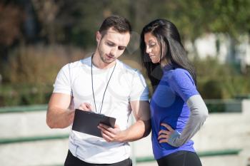 Personal Trainer Takes Notes While Young Woman Exercise in City Park Area - Training and Exercising for Endurance - Healthy Lifestyle Concept Outdoor