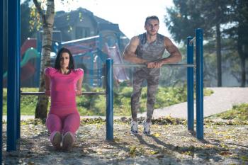 Attractive Couple Doing Crossfit Exercise With Dips Bar in City Park Area - Training and Exercising for Endurance - Healthy Lifestyle Concept Outdoor