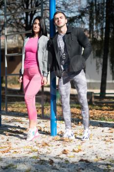 Fitness Couple Standing Strong  in City Park Area - Muscular Athletic Bodybuilder Model Posing After Exercises