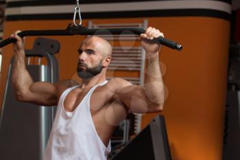 Handsome Bodybuilder Doing Heavy Weight Exercise For Back On Machine In Gym