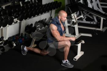 Muscular Man Stretching His Leg At The Floor In A Gym And Flexing Muscles - Muscular Athletic Bodybuilder Fitness Model