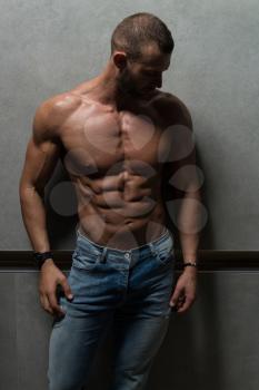 Healthy Young Man Standing Strong Standing Against a Wall and Flexing Muscles While Wearing Blue Jeans - Muscular Athletic Bodybuilder Fitness Model Posing After Exercises - a Place for Your Text