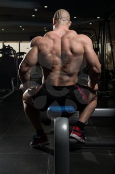 Young Man Sitting Strong In The Gym And Flexing Muscles - Muscular Athletic Bodybuilder Fitness Model Posing After Exercises