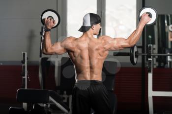 Healthy Young Man Standing Strong In The Gym And Flexing Muscles With Weights - Muscular Athletic Bodybuilder Fitness Model Posing After Exercises