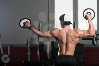 Healthy Young Man Standing Strong In The Gym And Flexing Muscles With Weights - Muscular Athletic Bodybuilder Fitness Model Posing After Exercises
