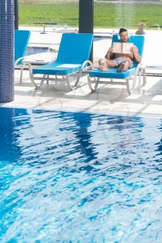 Young Man Resting On Sun Loungers By Swimming Pool and Listening Music On Headphones