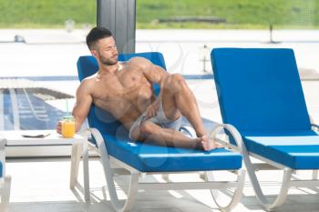 Young Man Resting On Sun Loungers By Swimming Pool With Orange Juice